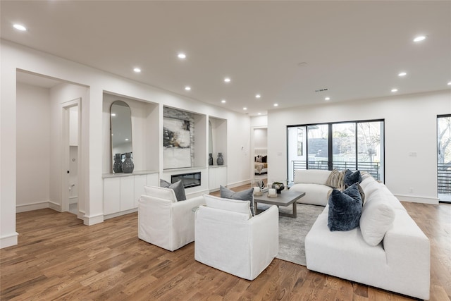 living room featuring recessed lighting, baseboards, a glass covered fireplace, and light wood finished floors