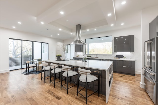 kitchen featuring modern cabinets, a tray ceiling, appliances with stainless steel finishes, island range hood, and light countertops