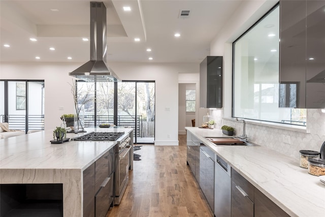 kitchen featuring visible vents, modern cabinets, island exhaust hood, a sink, and stainless steel stove