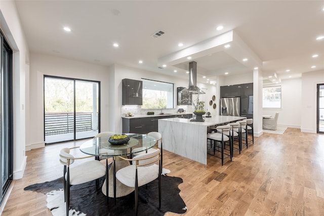 kitchen featuring island exhaust hood, stainless steel refrigerator with ice dispenser, modern cabinets, light wood-type flooring, and a center island