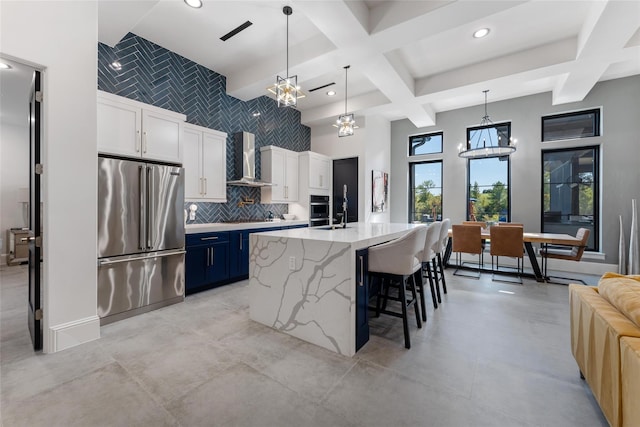 kitchen with coffered ceiling, stainless steel appliances, wall chimney exhaust hood, a notable chandelier, and backsplash