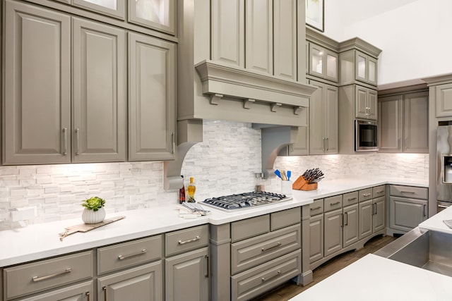 kitchen featuring custom exhaust hood, glass insert cabinets, gray cabinets, and appliances with stainless steel finishes