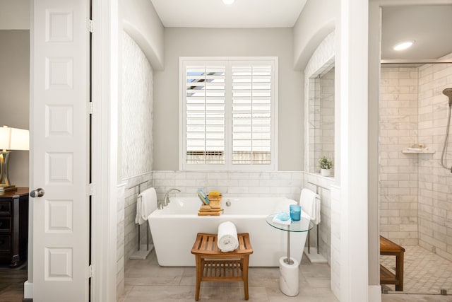 bathroom featuring a wainscoted wall, tiled shower, a freestanding bath, and tile walls