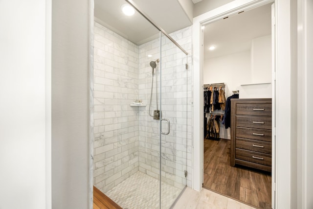 full bathroom with a spacious closet, a shower stall, and wood finished floors