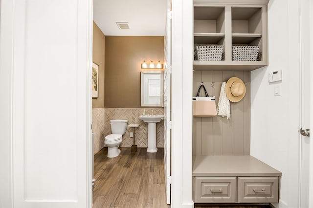 bathroom with wood finished floors, a wainscoted wall, visible vents, tile walls, and toilet