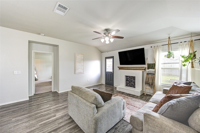 living room featuring visible vents, a fireplace with raised hearth, baseboards, vaulted ceiling, and wood finished floors