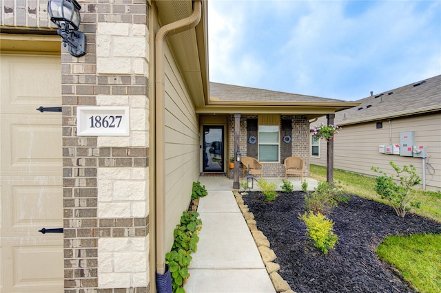 entrance to property with brick siding, a porch, an attached garage, and a shingled roof