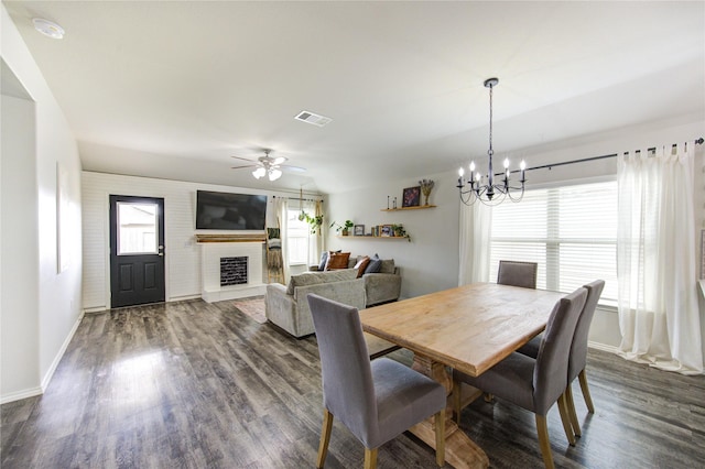 dining area with visible vents, a fireplace with raised hearth, baseboards, ceiling fan with notable chandelier, and dark wood-style floors