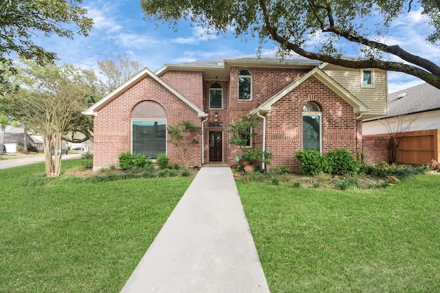 traditional-style house featuring brick siding, a front yard, and fence