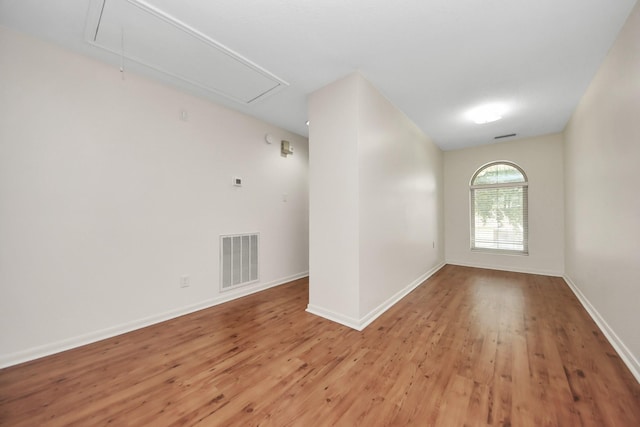 unfurnished room featuring visible vents, attic access, light wood-type flooring, and baseboards