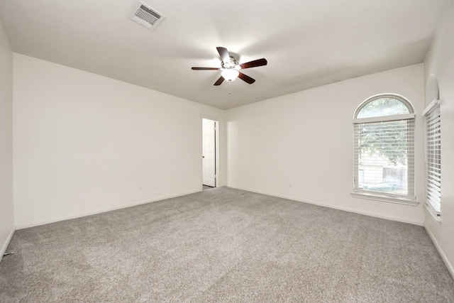 carpeted spare room with visible vents, baseboards, and ceiling fan