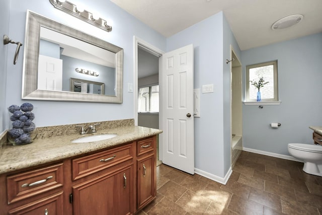 bathroom with vanity, toilet, baseboards, and stone finish flooring