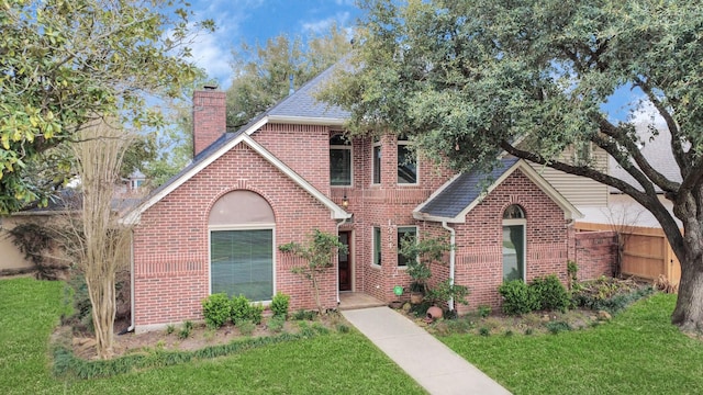 view of front of property with fence, roof with shingles, a chimney, a front lawn, and brick siding