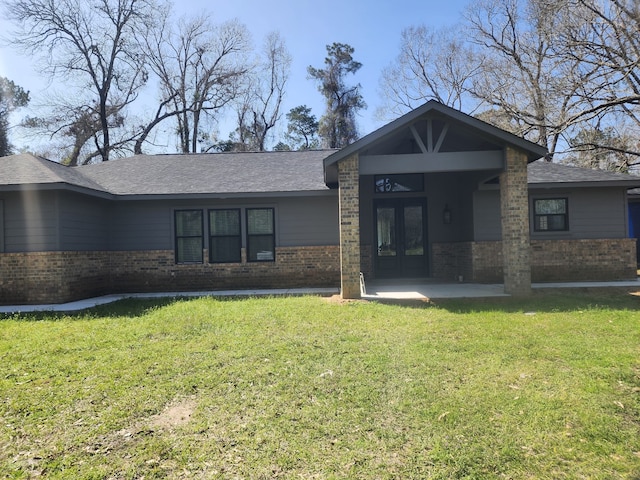 view of front of home featuring french doors, brick siding, roof with shingles, and a front yard