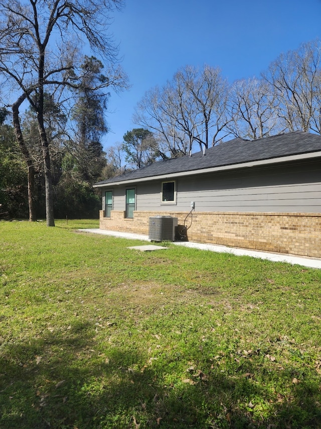 back of property with brick siding, central air condition unit, a shingled roof, and a yard