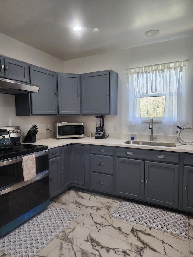 kitchen with under cabinet range hood, light countertops, appliances with stainless steel finishes, marble finish floor, and a sink