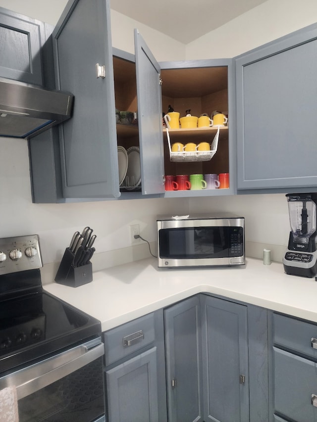 kitchen with gray cabinetry, light countertops, range hood, appliances with stainless steel finishes, and open shelves