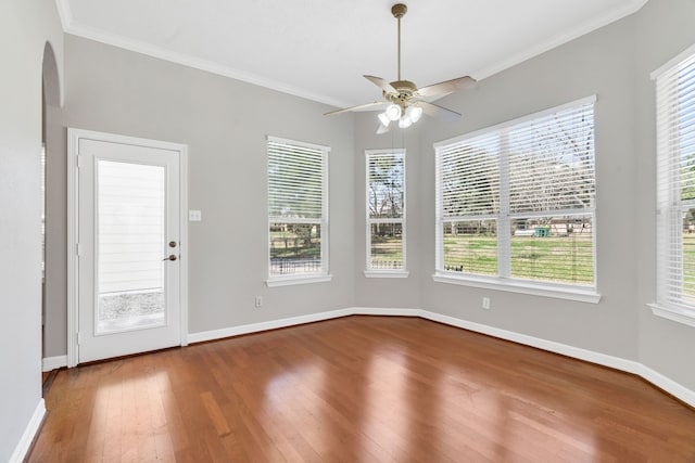 unfurnished dining area with crown molding, hardwood / wood-style flooring, arched walkways, and a wealth of natural light