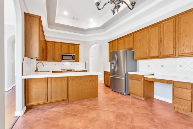 kitchen featuring a sink, arched walkways, appliances with stainless steel finishes, a peninsula, and a raised ceiling