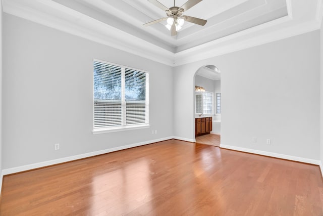 empty room with baseboards, a raised ceiling, arched walkways, and wood finished floors