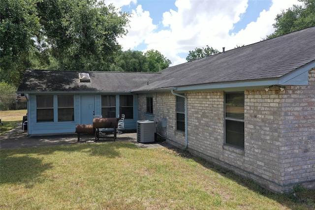 rear view of property featuring central air condition unit, a lawn, brick siding, and a shingled roof