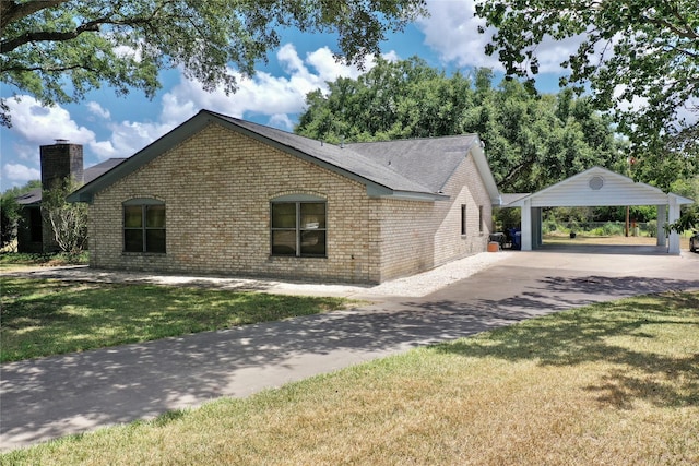 view of side of home with brick siding, concrete driveway, a lawn, a chimney, and a carport