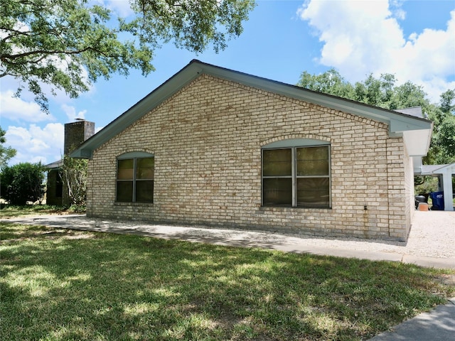 view of property exterior with brick siding, a lawn, and a chimney