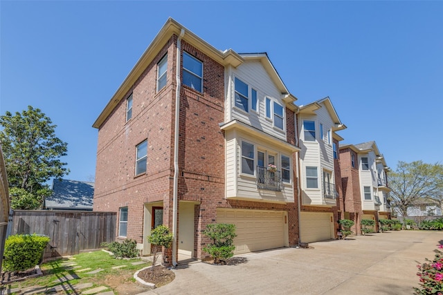 view of property exterior with brick siding, an attached garage, driveway, and fence