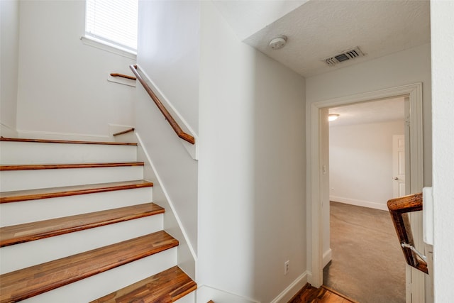 stairs with visible vents, baseboards, and a textured ceiling