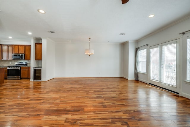 unfurnished living room featuring visible vents, baseboards, wood finished floors, and crown molding