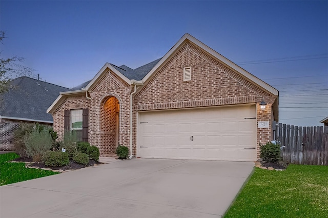 view of front facade featuring brick siding, an attached garage, driveway, and fence