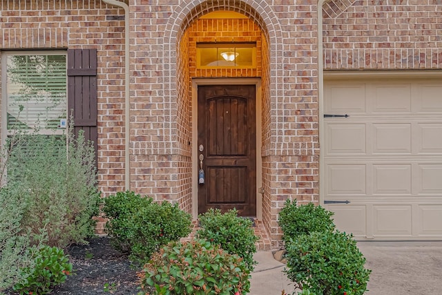 view of exterior entry featuring a garage and brick siding