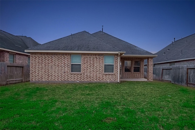 back of property with a yard, a fenced backyard, brick siding, and roof with shingles