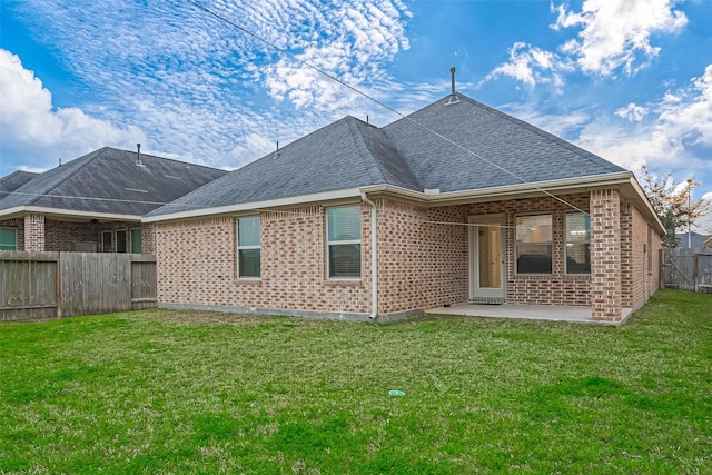 back of house with brick siding, roof with shingles, a fenced backyard, a yard, and a patio