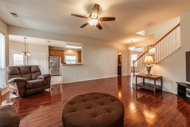 living area featuring wood finished floors, visible vents, baseboards, stairs, and ceiling fan with notable chandelier