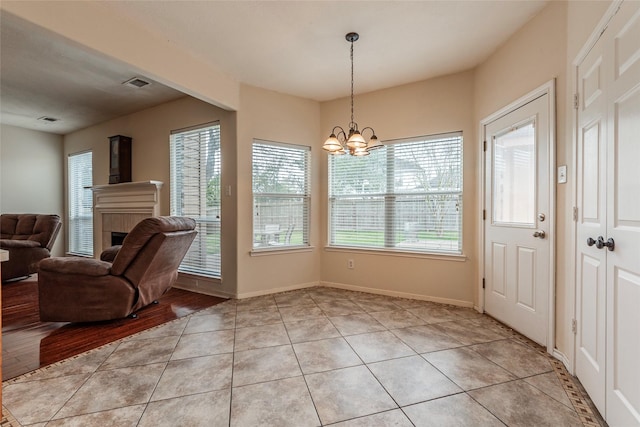 doorway to outside featuring a tiled fireplace, light tile patterned floors, visible vents, and a chandelier