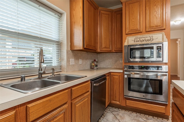 kitchen with brown cabinets, a sink, appliances with stainless steel finishes, light tile patterned flooring, and light countertops