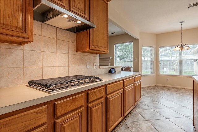 kitchen featuring visible vents, backsplash, under cabinet range hood, stainless steel gas cooktop, and brown cabinetry