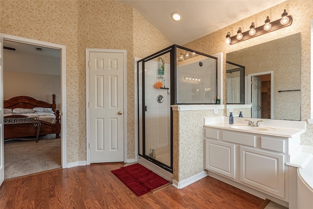 bathroom featuring wood finished floors, a shower stall, wallpapered walls, lofted ceiling, and vanity