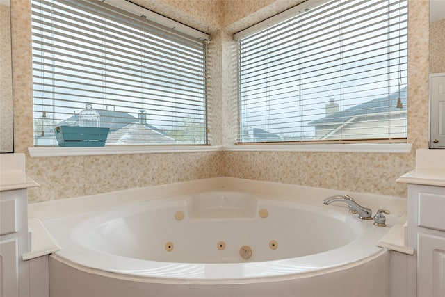 bathroom with a tub with jets, wallpapered walls, and vanity