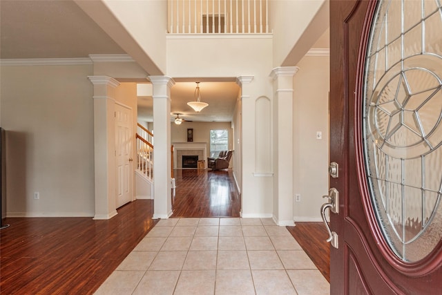 tiled foyer entrance featuring a tiled fireplace, baseboards, crown molding, and ornate columns