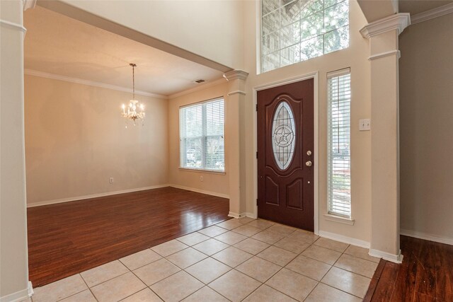 entrance foyer with crown molding, light tile patterned floors, ornate columns, and a chandelier