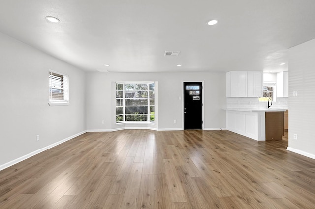 unfurnished living room featuring wood finished floors, visible vents, baseboards, recessed lighting, and a sink