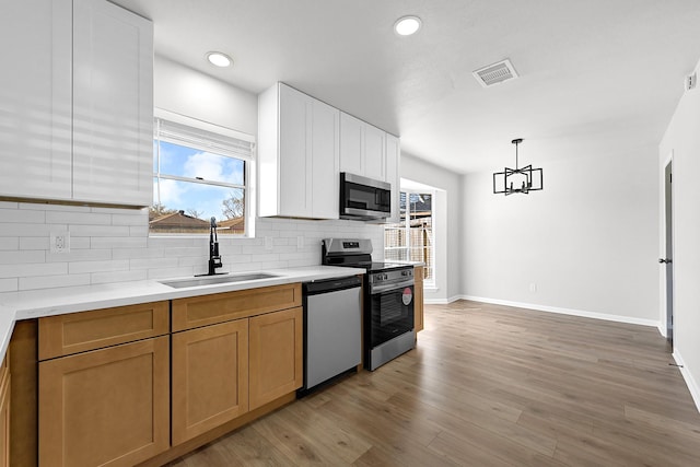 kitchen with light wood finished floors, light countertops, decorative backsplash, appliances with stainless steel finishes, and a sink