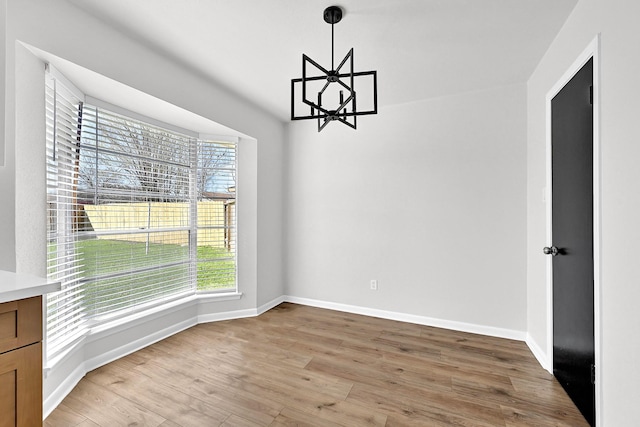 unfurnished dining area with an inviting chandelier, light wood-type flooring, and baseboards