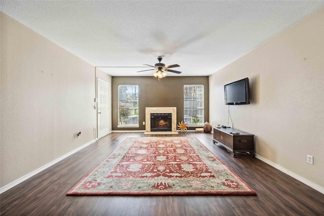 unfurnished living room featuring wood finished floors, baseboards, ceiling fan, a lit fireplace, and a textured ceiling