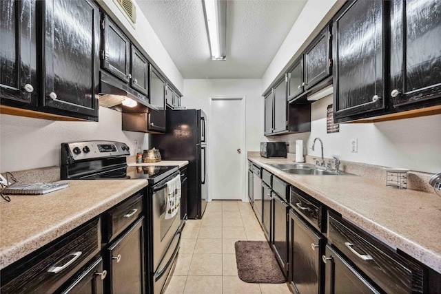 kitchen featuring a sink, stainless steel appliances, light tile patterned flooring, a textured ceiling, and dark cabinets