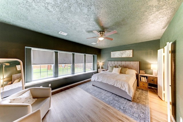 bedroom with a ceiling fan, wood finished floors, visible vents, and a textured ceiling