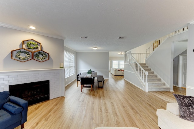 living area with stairway, light wood-style flooring, a fireplace, ornamental molding, and a textured ceiling