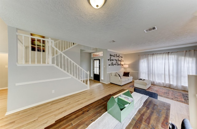 living room with stairs, wood finished floors, visible vents, and baseboards